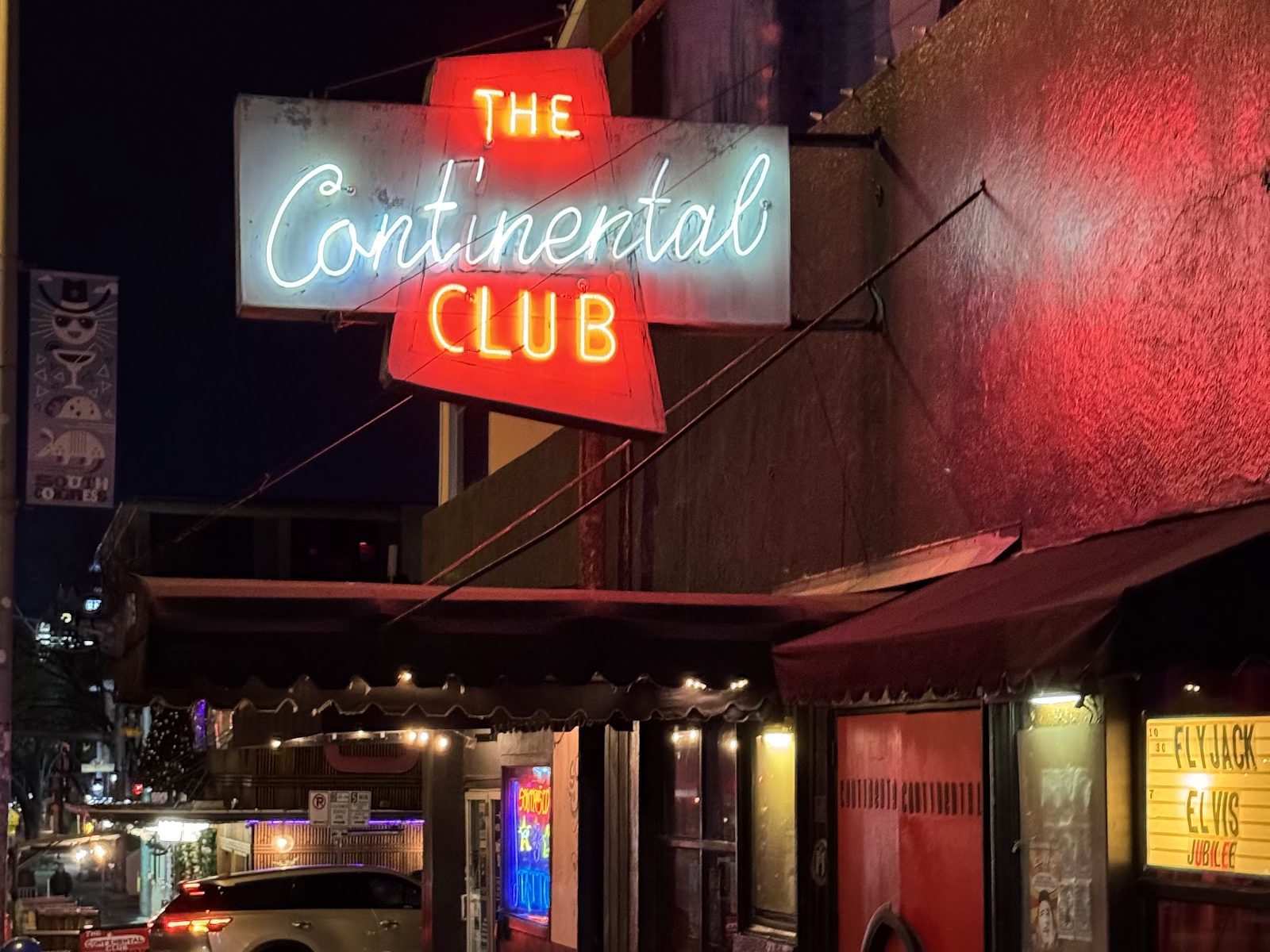 The Continental Club at night: its neon sign in red and white script above a scalloped awning, a red front door and a lit marquee on South Congress