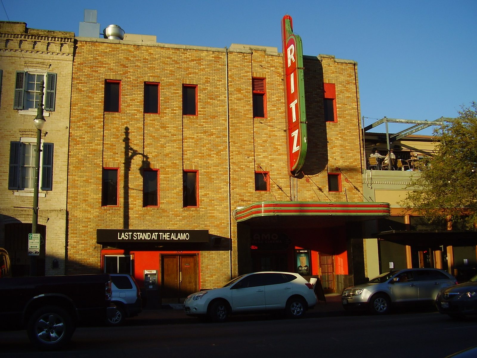 The Ritz on Sixth Street in Austin: a tan brick theater with a vertical red RITZ neon sign, a striped marquee and cars parked along the curb