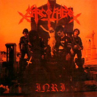 Cover of Sarcófago’s I.N.R.I.: four band members in corpsepaint and bullet belts in a cemetery at night, a crucifix behind them, all washed in orange-red light