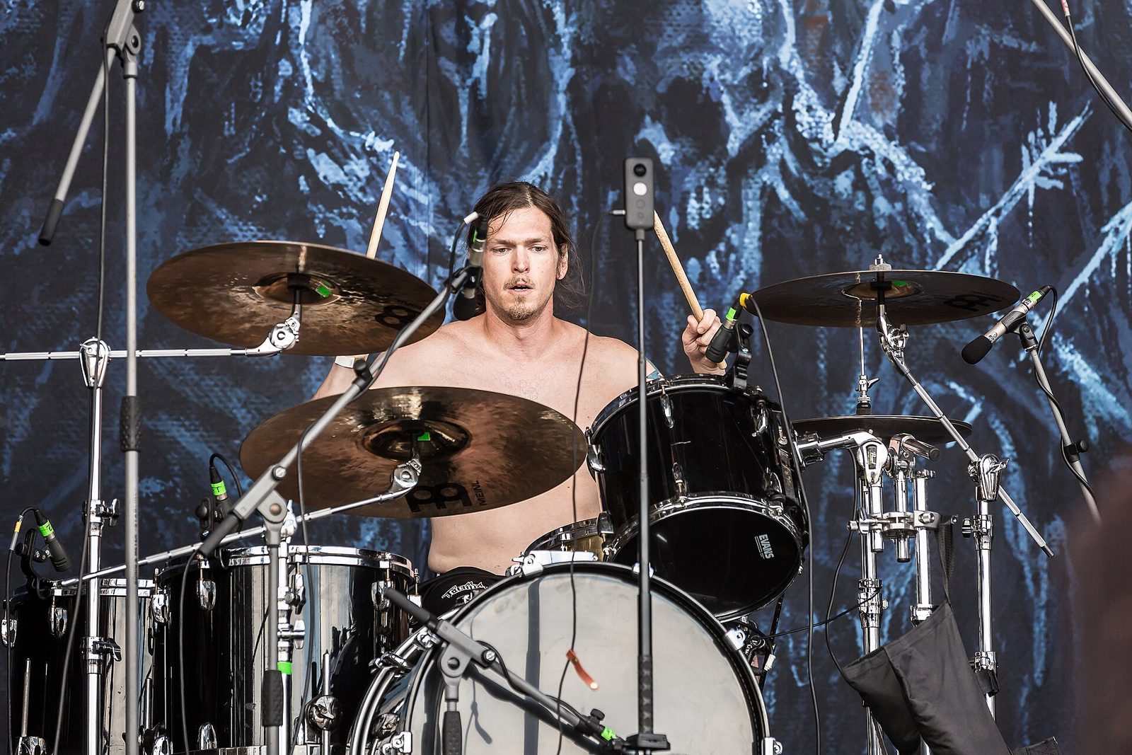Frozen Soul's shirtless drummer behind a black drum kit and bronze cymbals, an icy blue painted backdrop behind him