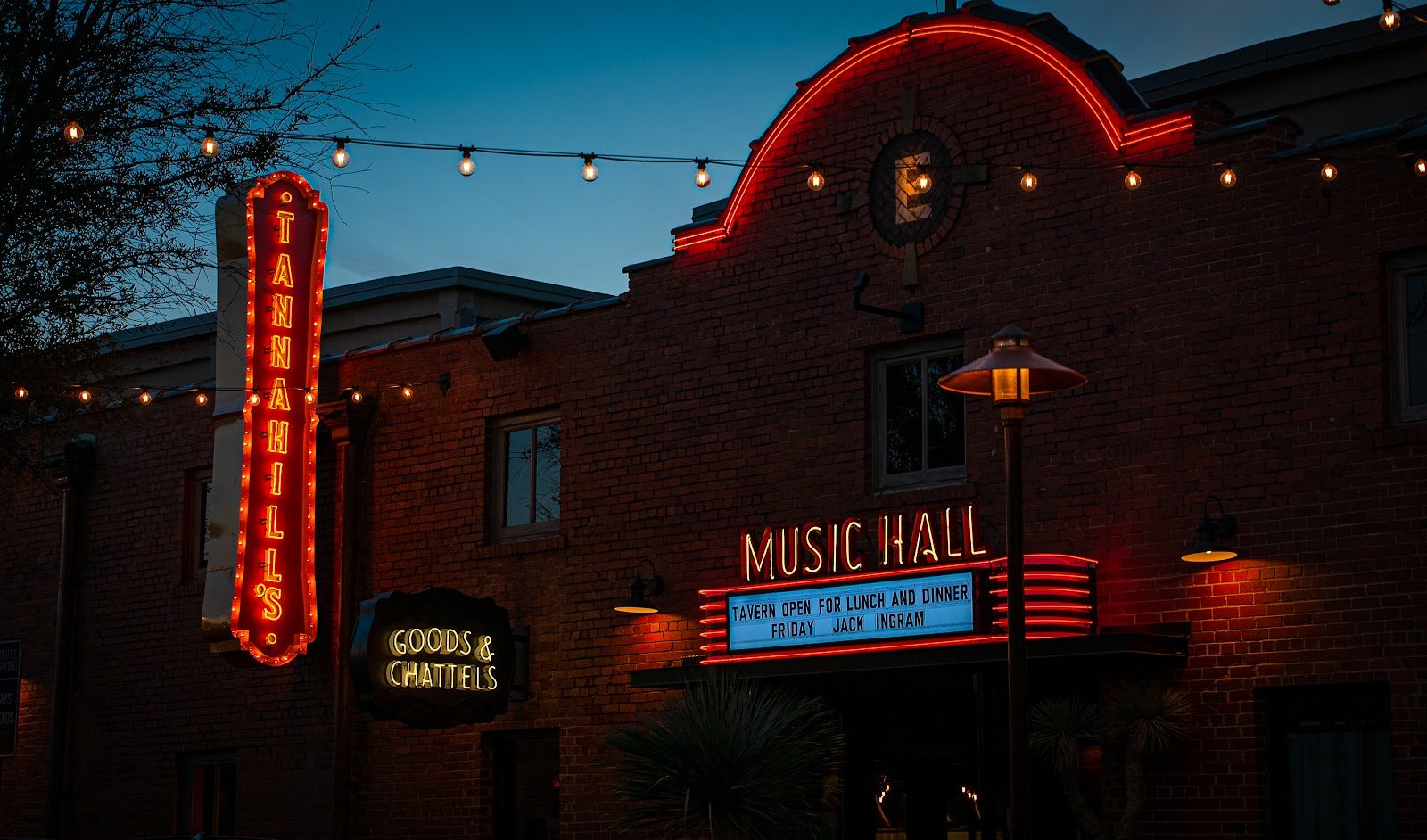 Tannahill's brick music hall at dusk, a tall red neon Tannahill's sign at left and a lit Music Hall marquee over the entrance, string lights across the facade