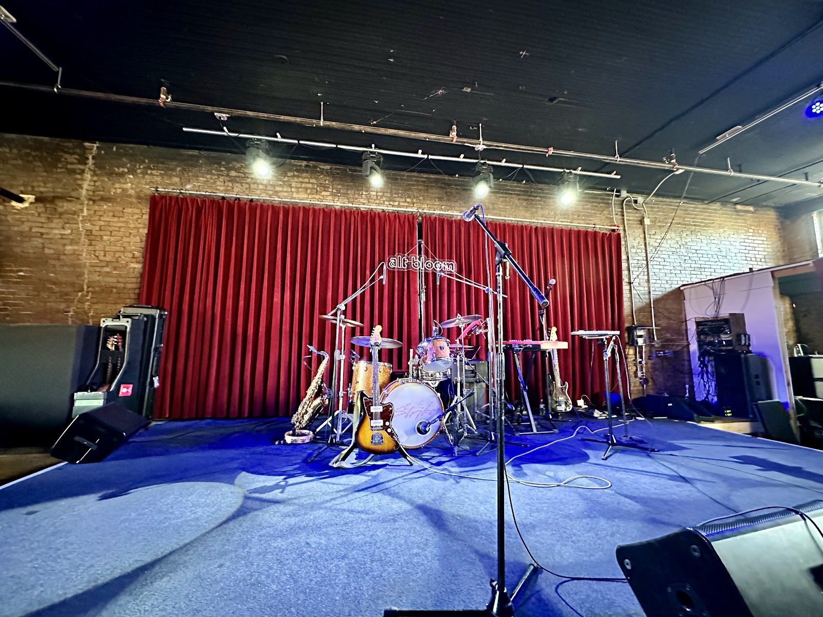The empty Club Dada stage set with drums, guitars and a saxophone in front of a red velvet curtain and a brick wall