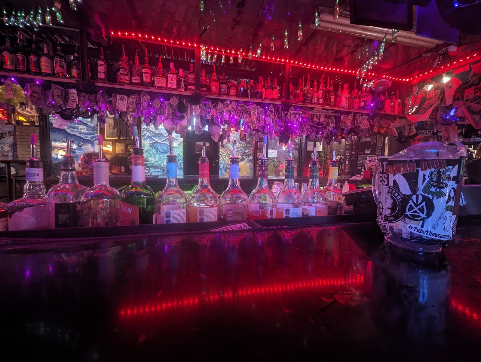 The back bar at Reno's Chop Shop lit in red and purple, with a row of liquor bottles and dollar bills pinned along the shelves