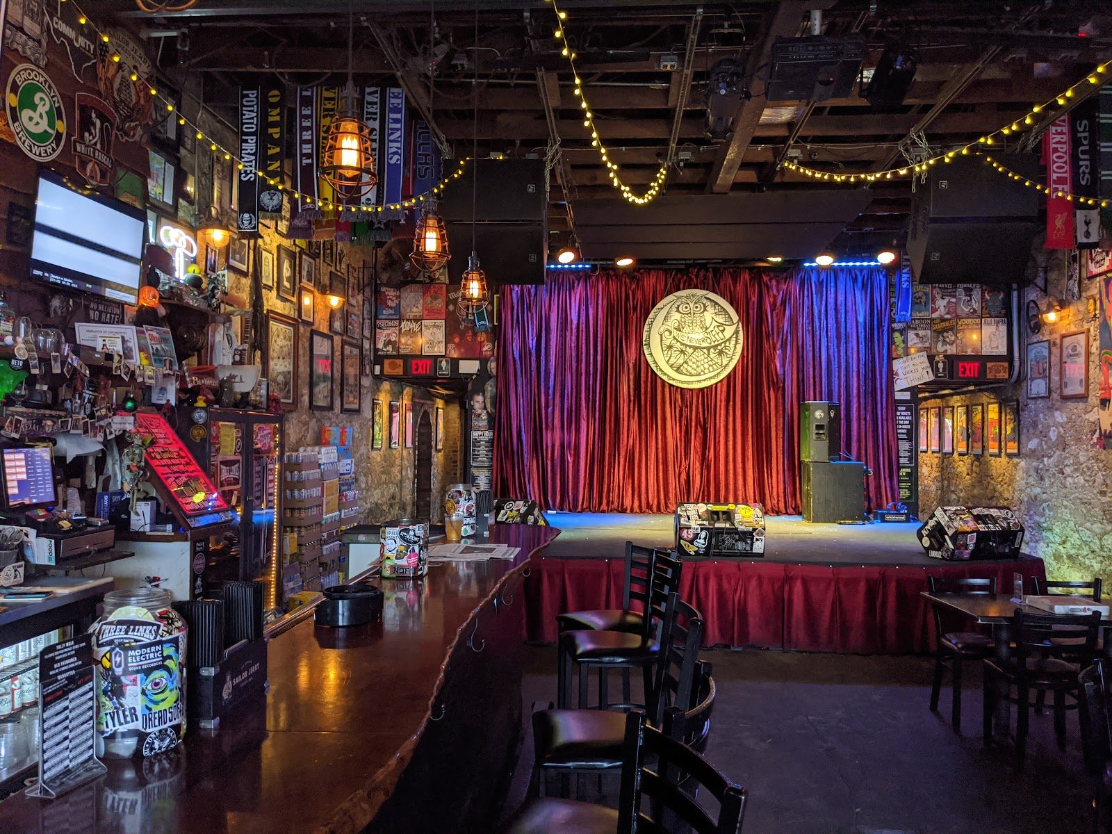 Inside Three Links: a long wooden bar covered in stickers on the left, and a small stage with a red curtain and an owl emblem at the back