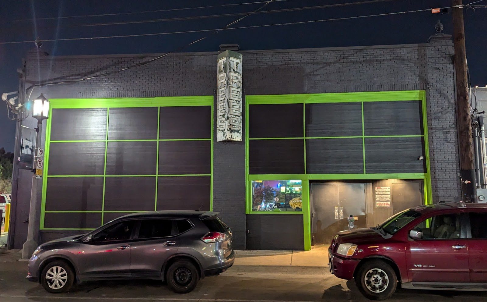 The black brick front of Trees on Elm Street at night, with green-trimmed windows and a tall vertical TREES sign