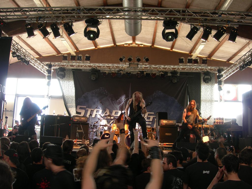 Strapping Young Lad on a festival stage under a lighting rig, with the band's banner behind them and a crowd raising their hands in front