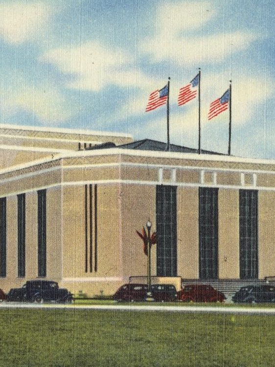 Linen postcard of the Sam Houston Coliseum and Music Hall around 1940: a long cream art deco building with tall dark windows, flags on the roof and old cars parked out front