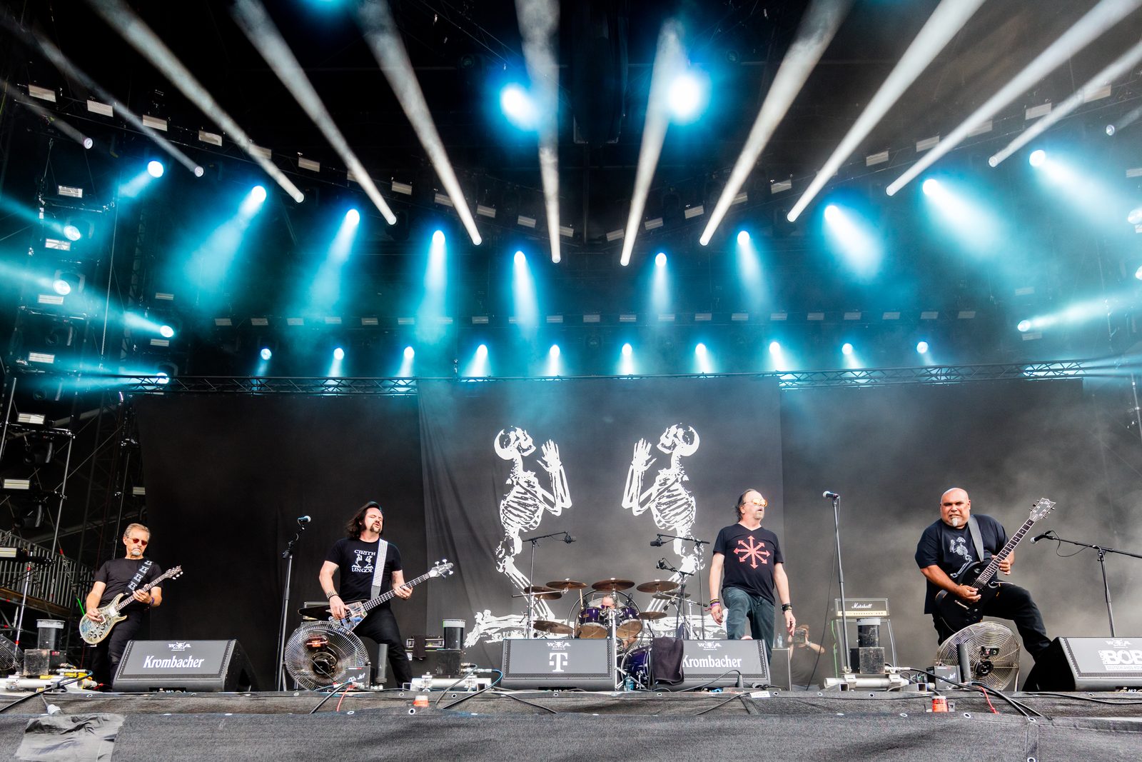 Cirith Ungol's five members performing on a large outdoor festival stage under blue spotlights, with two skeleton figures on the backdrop