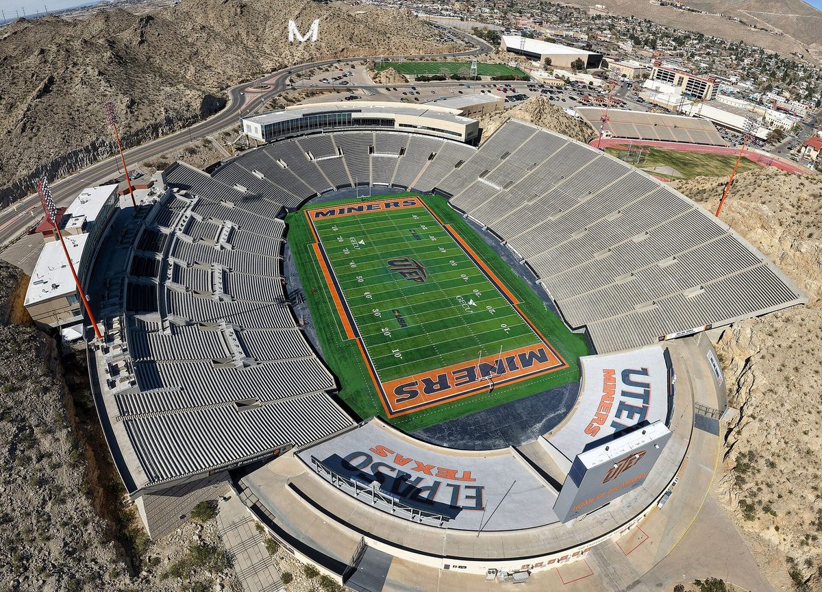 Aerial view of Sun Bowl Stadium in El Paso: a horseshoe of grey seats cut into a rocky hillside around a green field painted Miners in the end zones, with the white M on the mountain behind