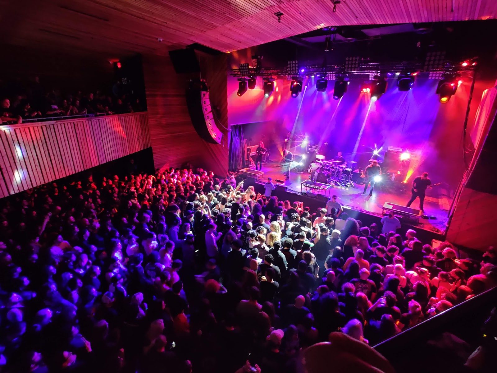 View from the balcony of White Oak Music Hall’s indoor room: a packed floor facing a band on a stage lit pink and purple, wood-slatted walls and ceiling