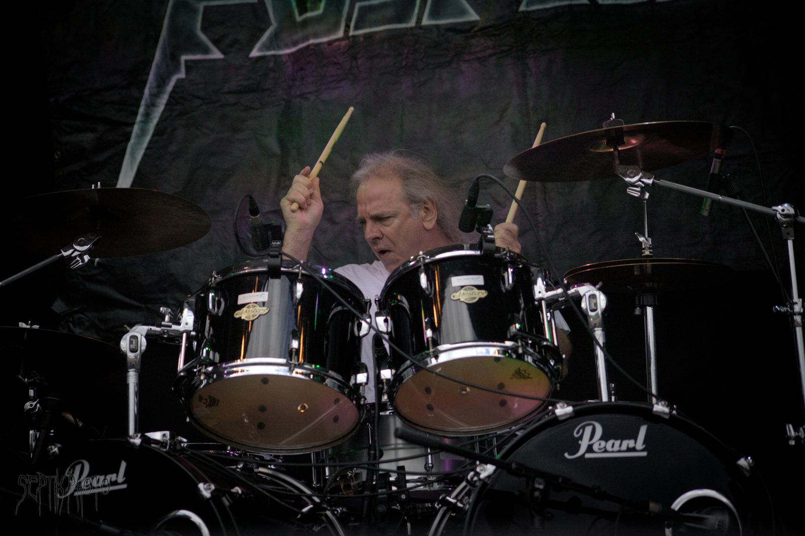 Glenn Evans behind a black Pearl drum kit, sticks raised, with the Nuclear Assault logo banner behind him