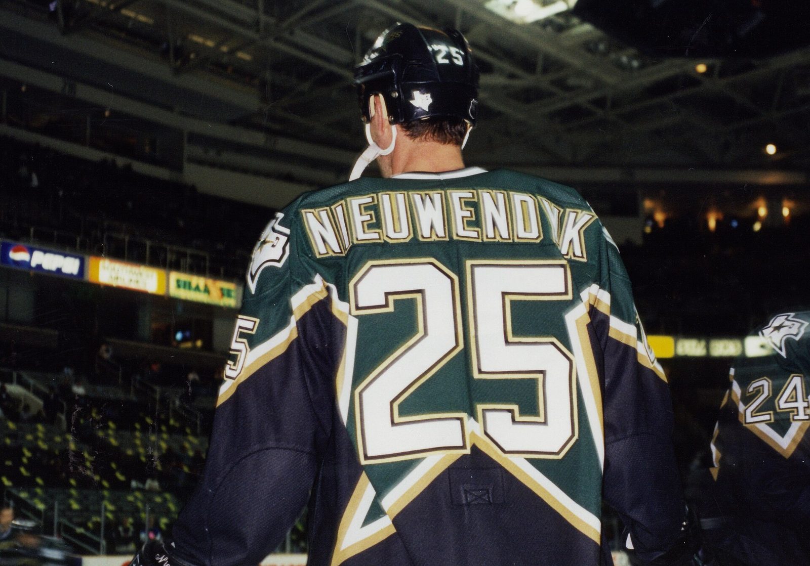 Joe Nieuwendyk, seen from behind in a green, black and gold Dallas Stars jersey with the number 25, standing on the ice in an arena