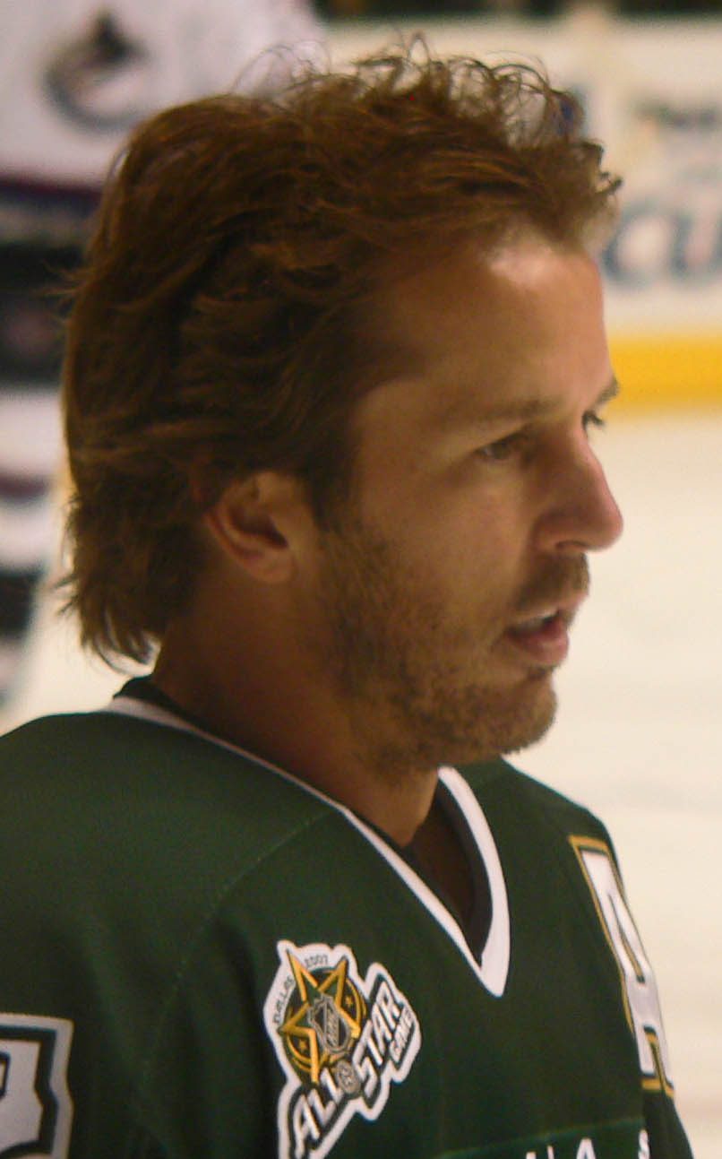 Mike Modano in profile, with long reddish hair and a beard, wearing a green Dallas Stars jersey on the ice
