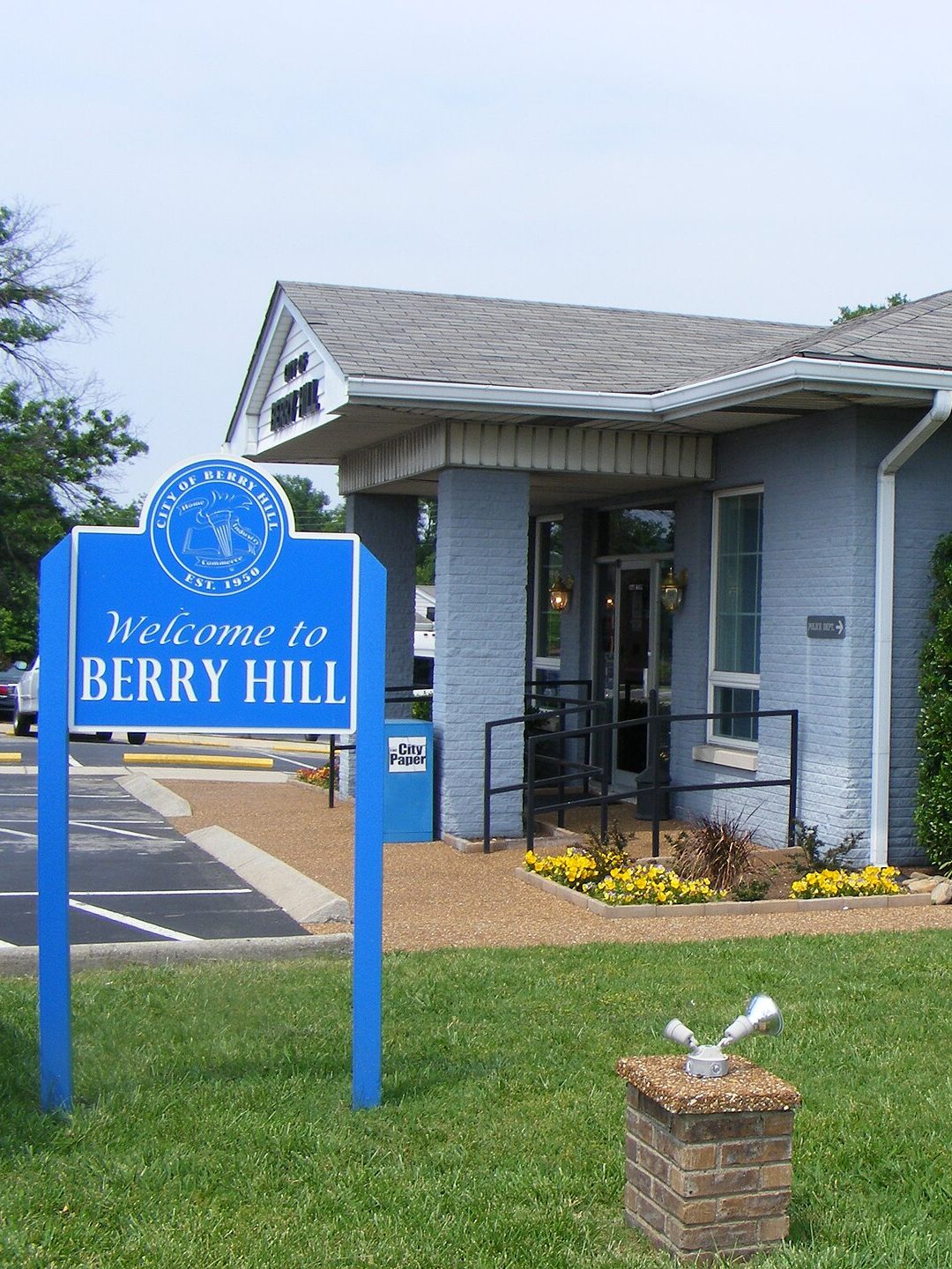 A blue Welcome to Berry Hill sign on a lawn beside the entrance of Berry Hill's gray-blue brick city hall