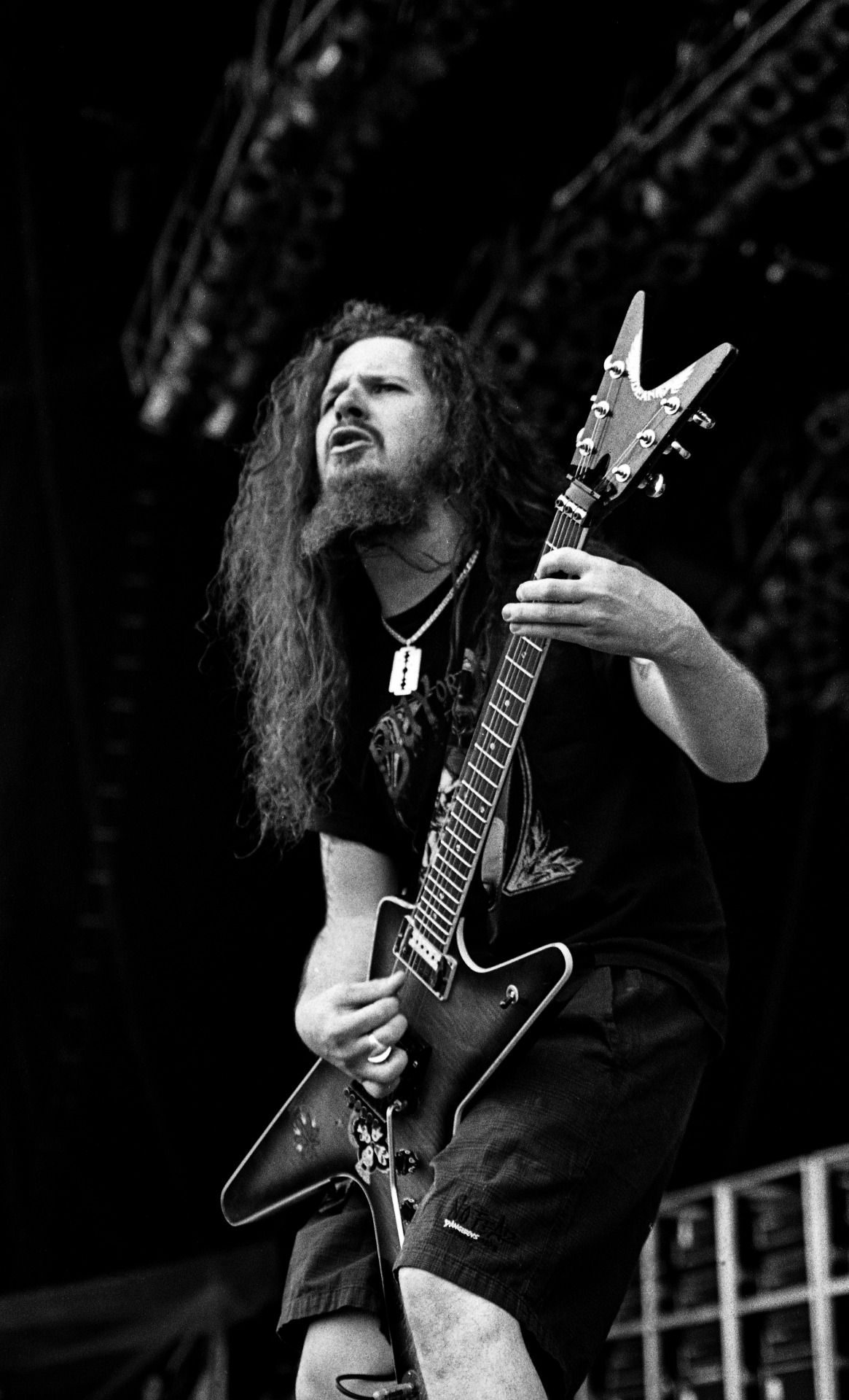 Black-and-white photo of Dimebag Darrell, long-haired and bearded, playing an angular, pointed guitar on an outdoor festival stage