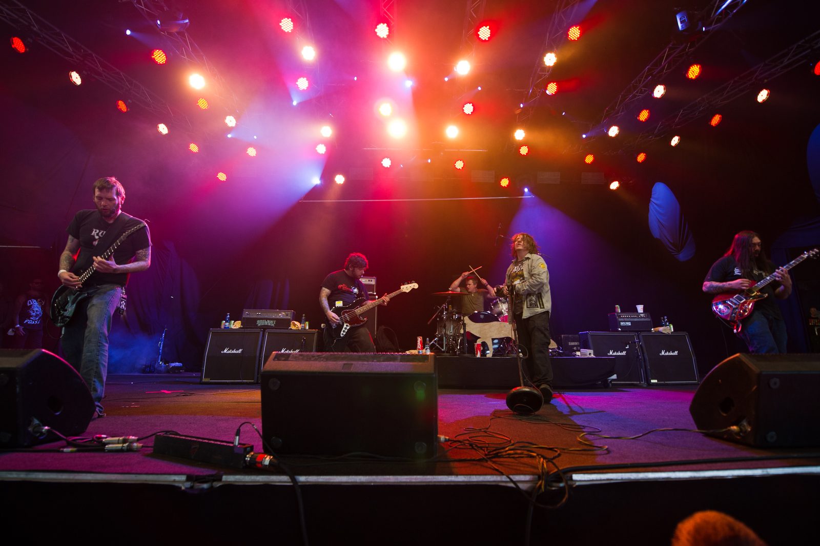 Eyehategod performing on an outdoor stage under red and orange lights, two guitarists and a bassist flanking the singer, with Marshall cabinets behind
