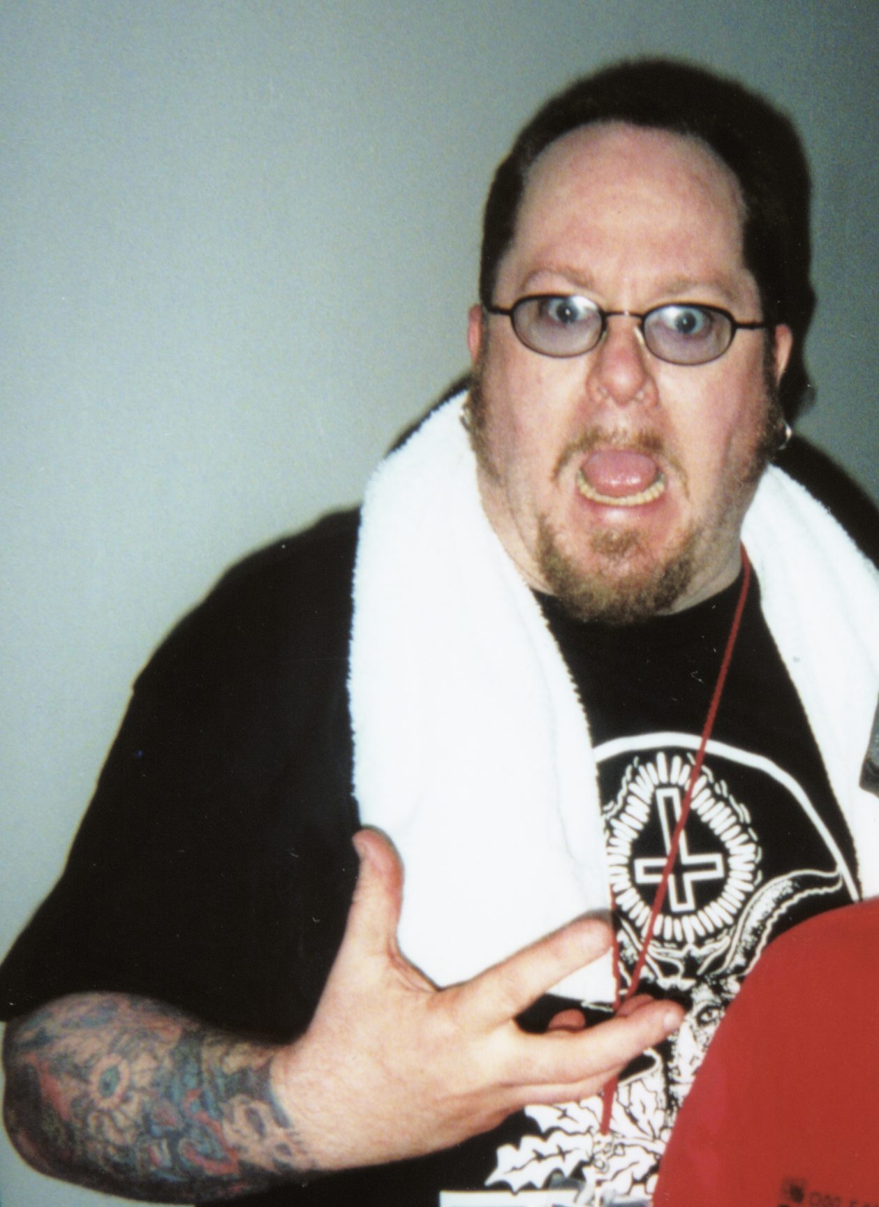 Casey Orr in glasses and a black T-shirt with a white towel around his neck, pulling a face at the camera