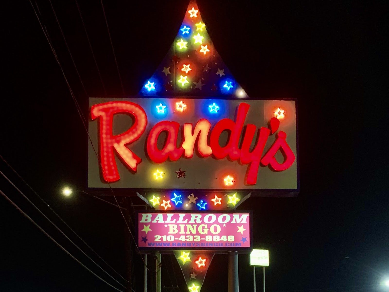 The tall lit roadside sign for Randy's on Bandera Road at night, red script letters ringed with colored neon stars above a pink panel reading Ballroom Bingo