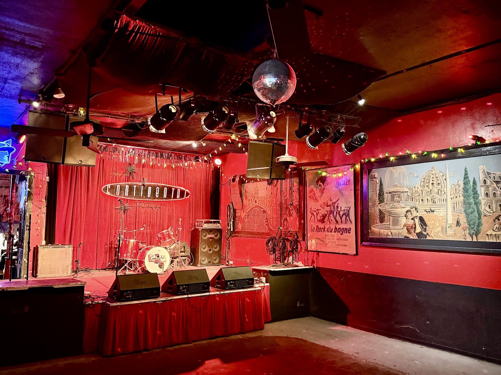 The Continental Club's empty stage under red lights, with a red curtain, a disco ball and the club's Continental sign behind the drum kit