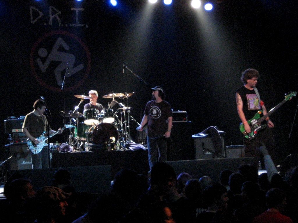 D.R.I. performing under blue and white stage lights, D.R.I. banner behind them, 2010