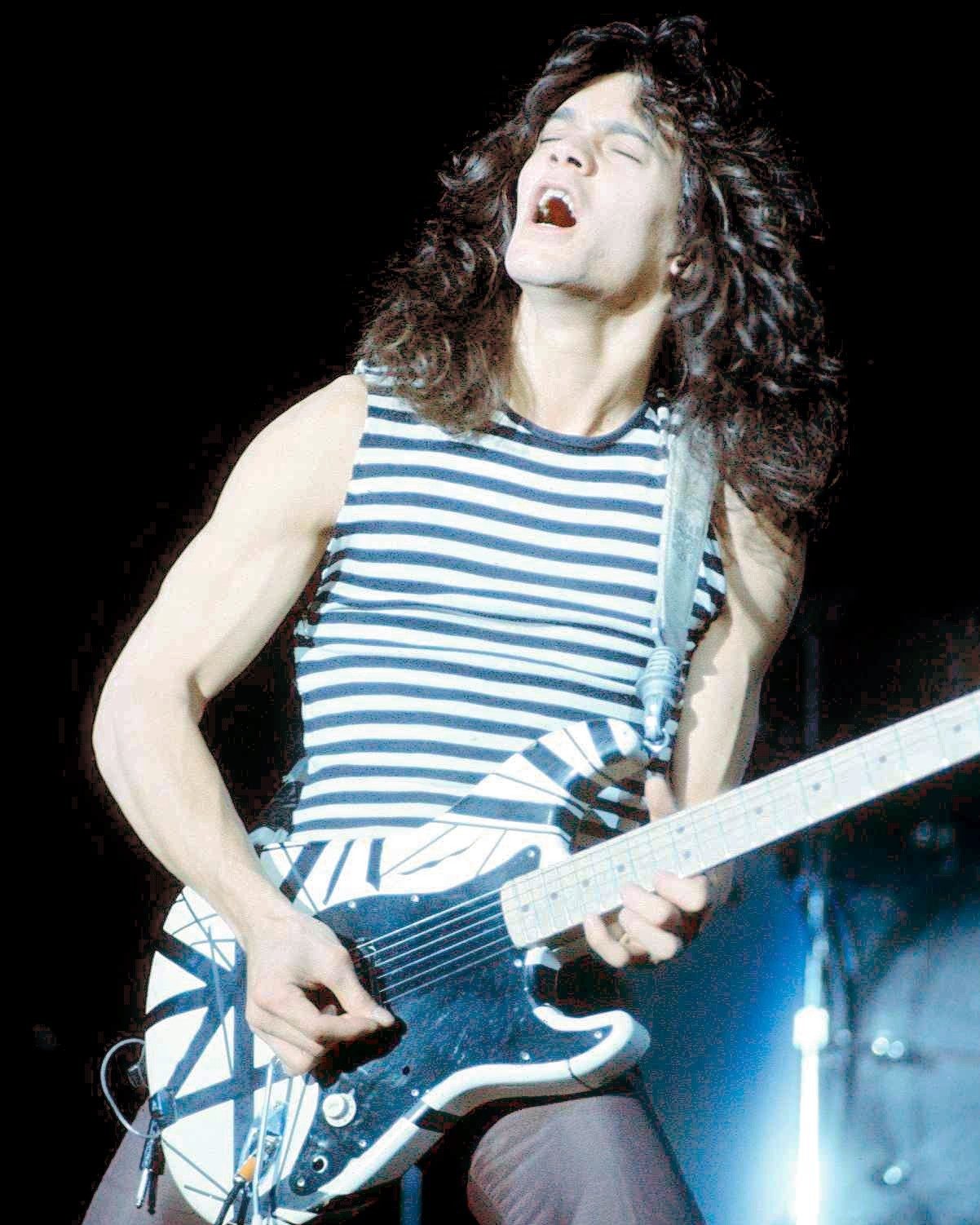 Eddie Van Halen in a striped sleeveless shirt, head thrown back, playing his black-and-white striped guitar on stage